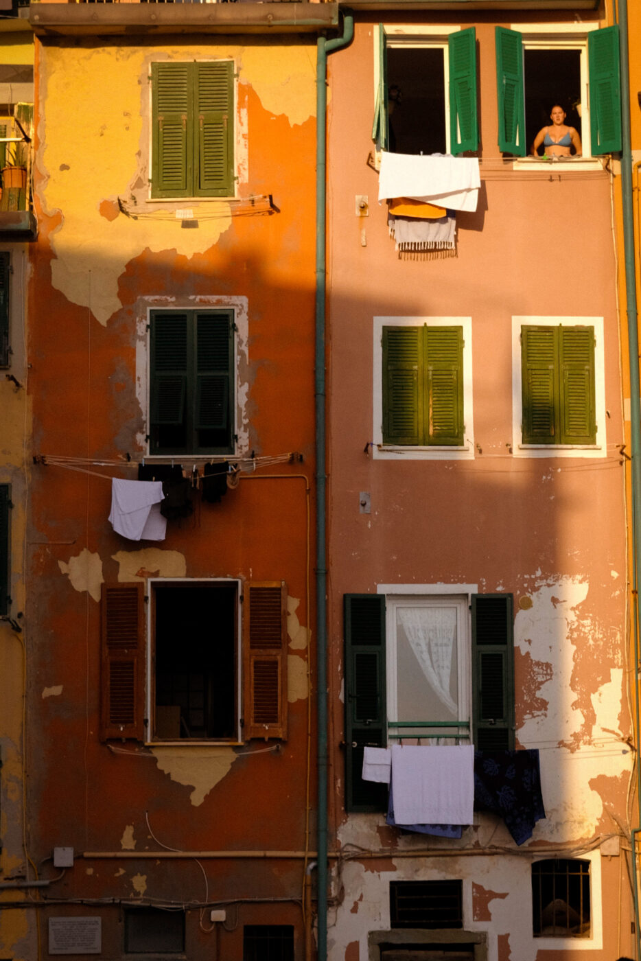 An image of a bright orange house in Cinque Terre with a woman in a bathing suit looking out the window