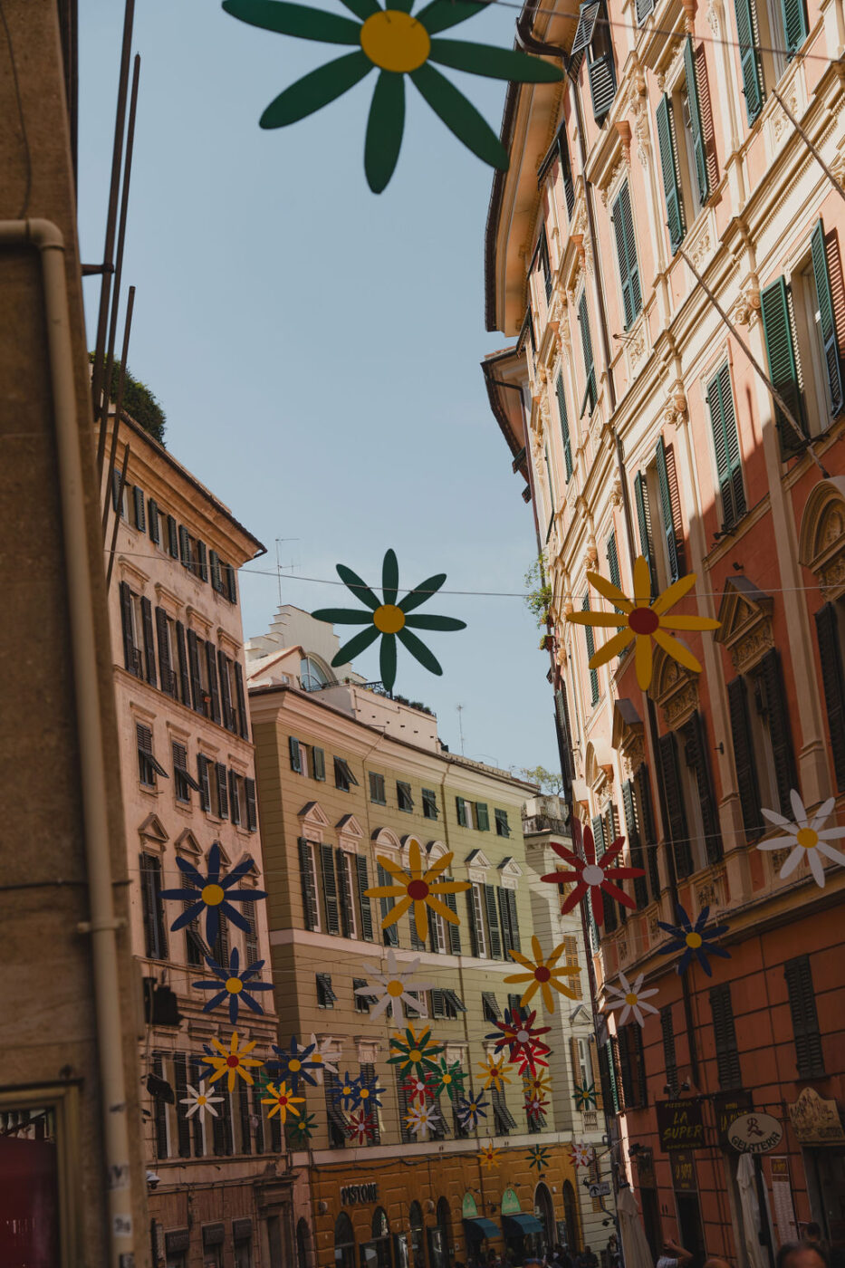 an image of a thin street in Genova with colorful houses and flowers strung on strings between the houses