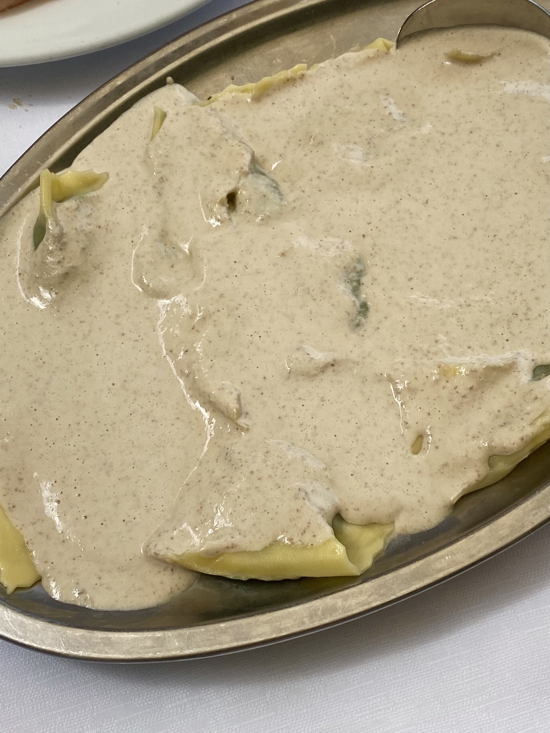 Pansotti (ravioli) with beige Salsa di Noci on a silver platter
