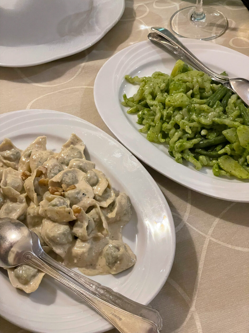 an image of two plates of pasta, one is pansotti with noci sauce and one is trofie with pesto