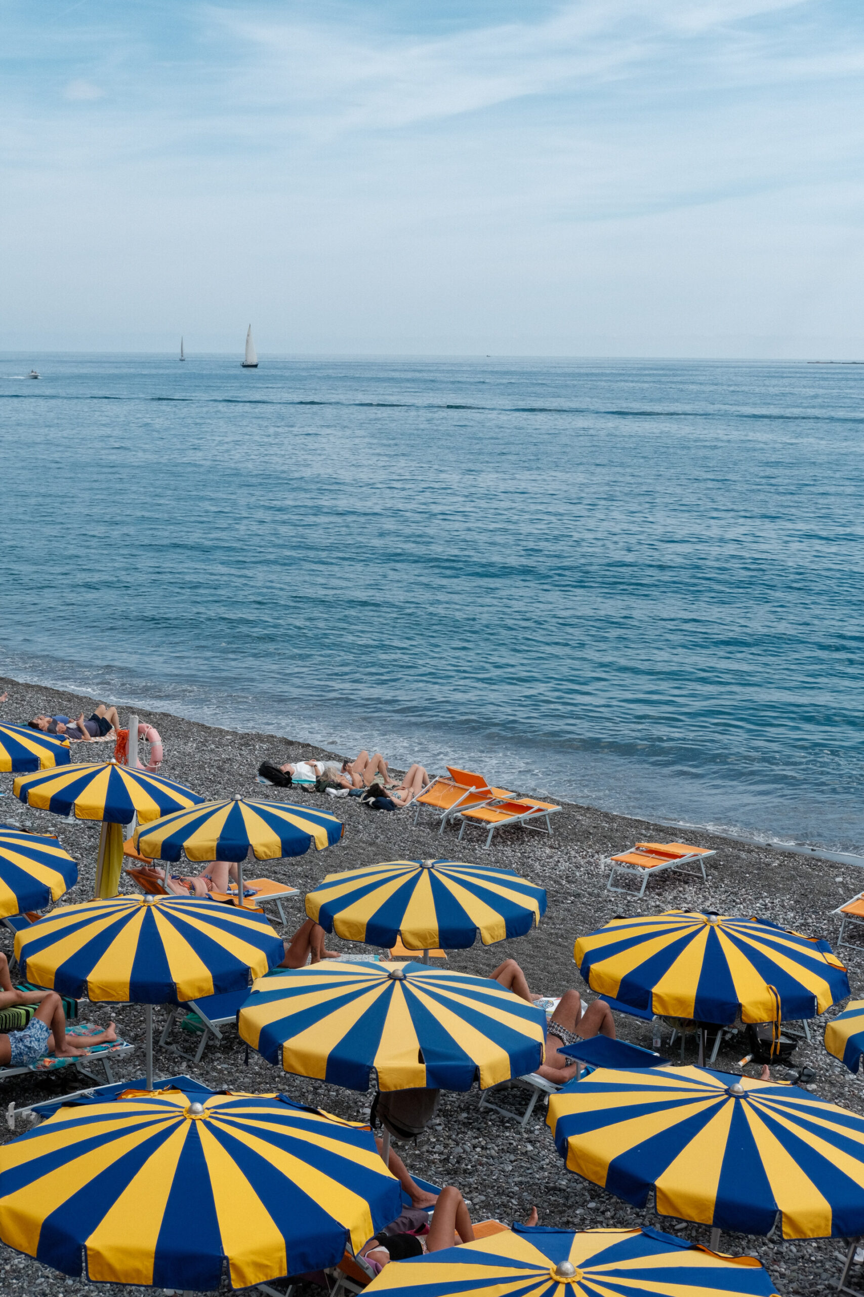 an image of the seaside in Chiavari with yellow and blue stripped umbrellas and people lying on the rocky beach