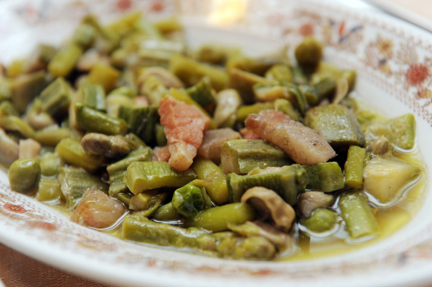 a close up of vignarola, a spring warm salad with green veggies and guanciale