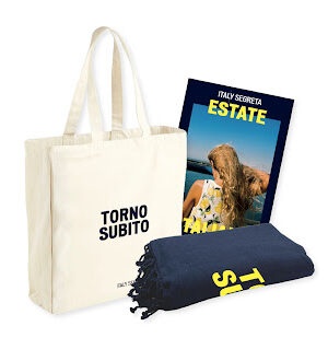 The Estate Italiana Red Bundle - The image shows a beige tote bag with TORNO SUBITO printed on the front, a rolled-up navy blanket, and an ITALY SEGRETA ESTATE magazine that features a woman standing by the sea.