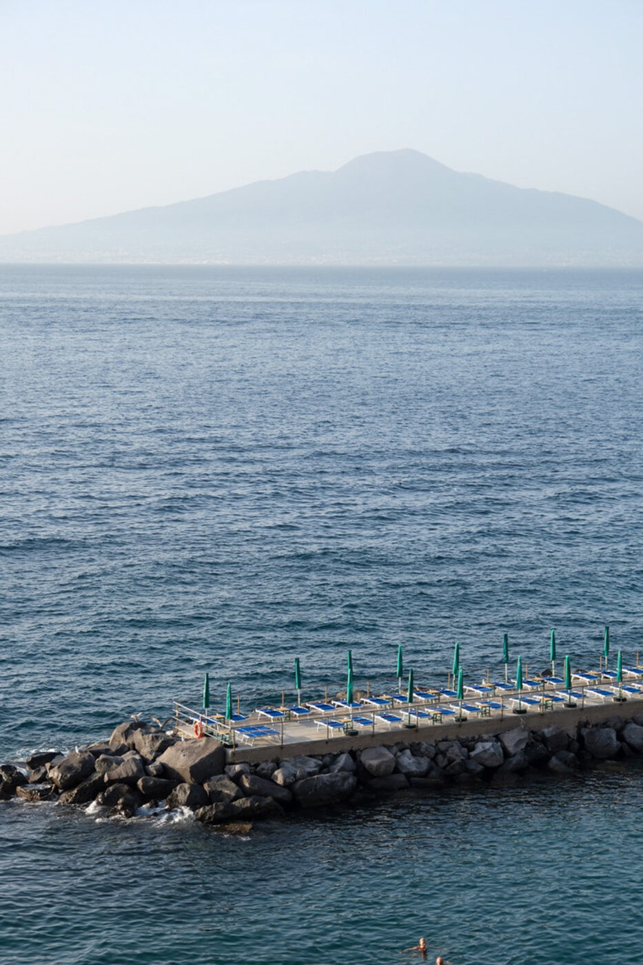 a long bagno with lounge chairs on a rocky peninsula sticking out into the bay in front of Vesuvius