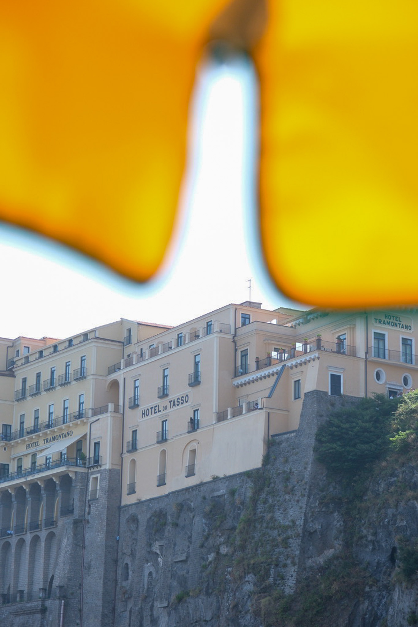 a photo taken from under a yellow beach umbrella of hotels on the rocky cliffs of sorrento