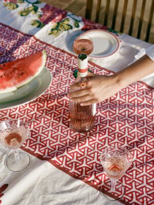 an image of a woman grabbing a bottle of rose with a nice ring on and a table with watermelon
