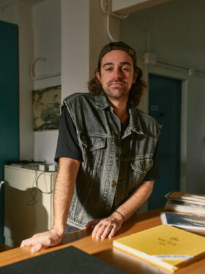 an image of Glauco Canalis standing in his studio leaning on a table in a vest