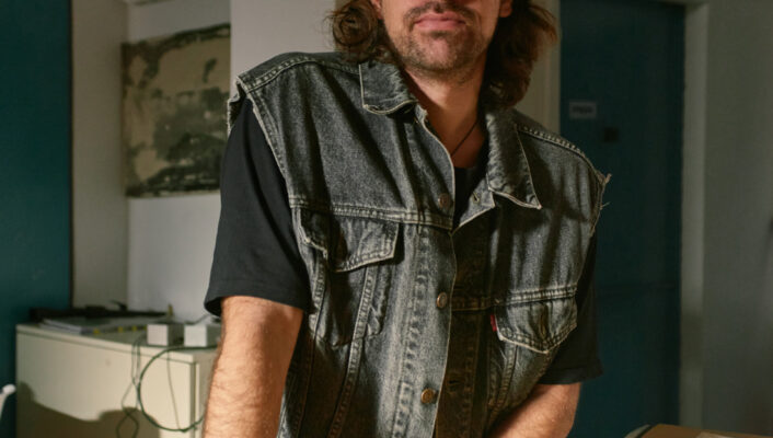 an image of Glauco Canalis standing in his studio leaning on a table in a vest