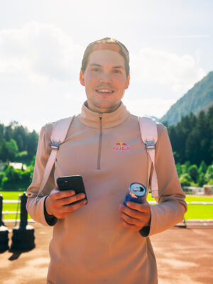 an image of a man with a red bull and his phone wearing a backwards hat and a quarter zip ready to go skiing