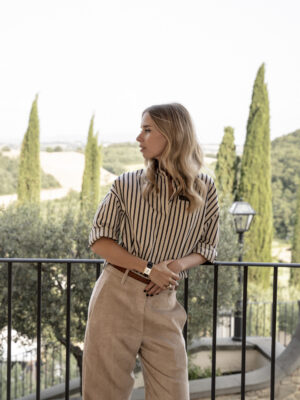 an image of carolina cucinelli in a stripped shirt leaning against an iron railing with blond curled hair