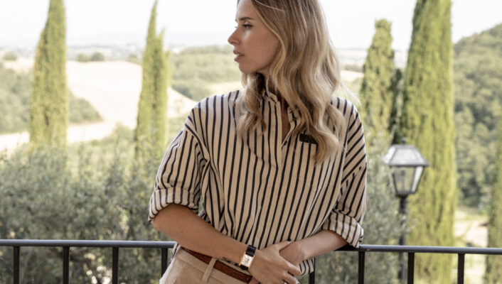 an image of carolina cucinelli in a stripped shirt leaning against an iron railing with blond curled hair