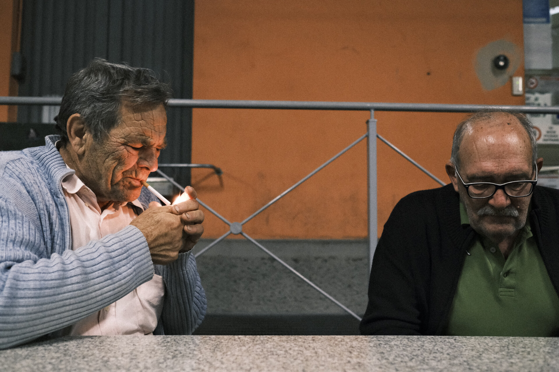 two men sitting at the cooperative, one is lighting a cigarette