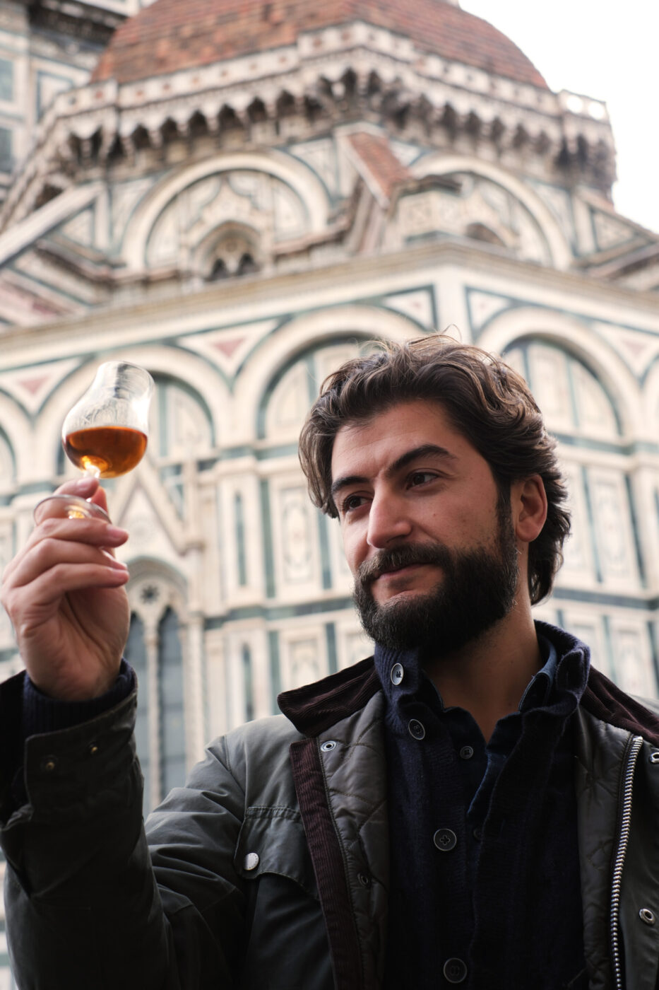 a man holding a glass of whiskey and admiring it in front of the duomo in Florence