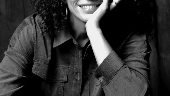 a black and white image of a girl with glasses and curly hair sitting and resting her chin in her hand