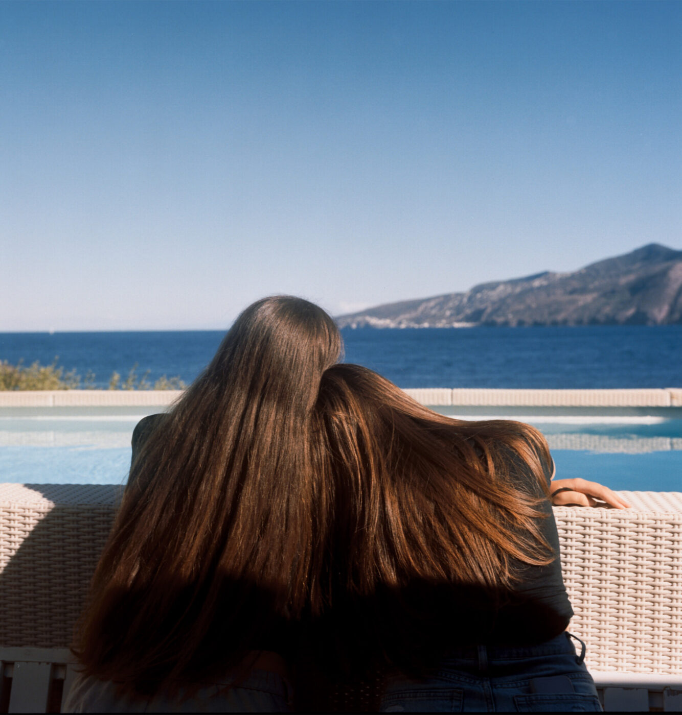 an image from behind of two girls with their heads on each others' shoulders while riding a ferry
