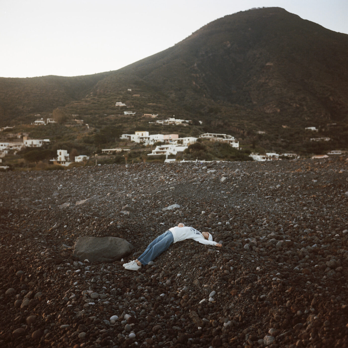 an image of a teen lying on his back in the rocks on a beach in front of a volcano