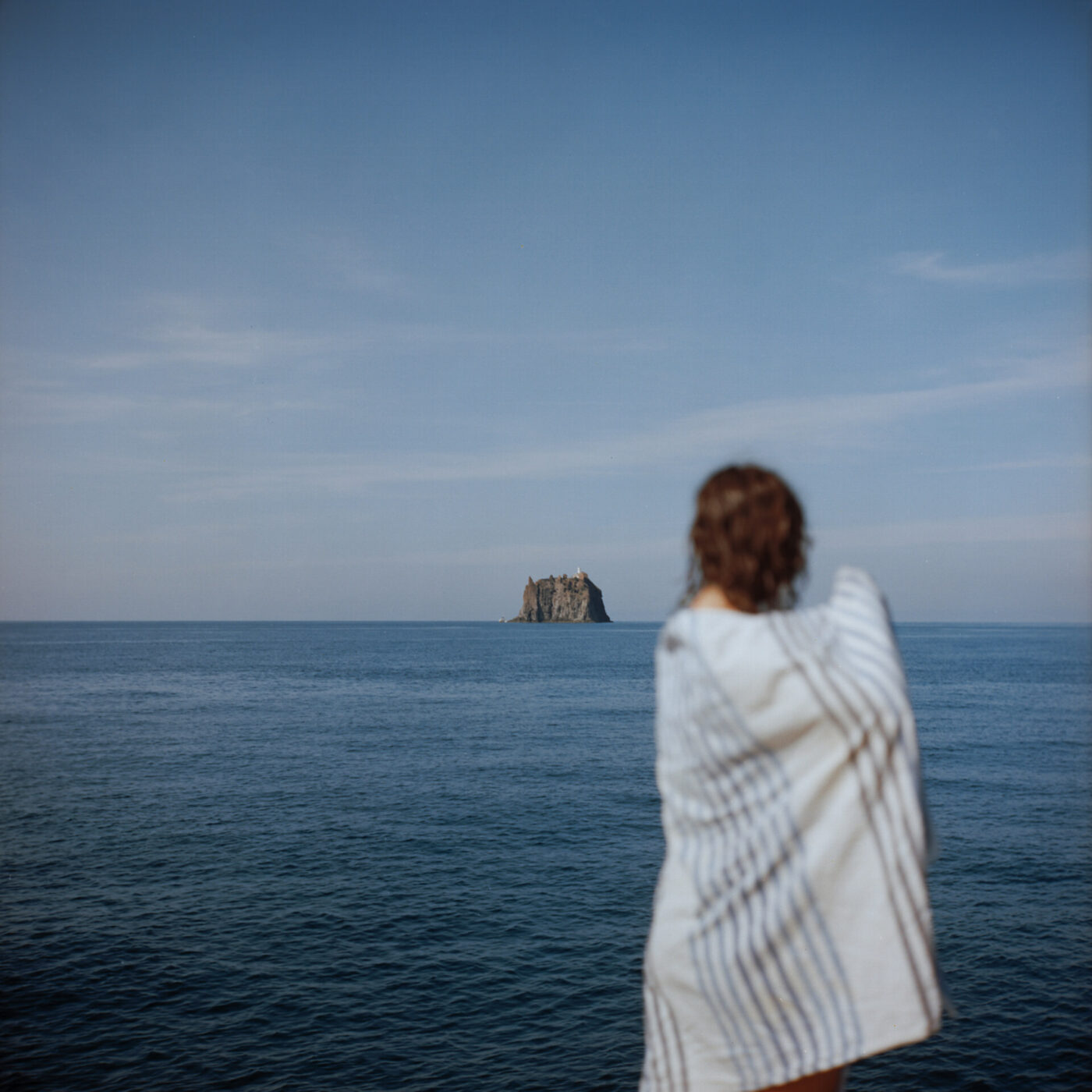 an image of a blurry teen wrapped in a beach towel on the coast with a tiny island off in the distance