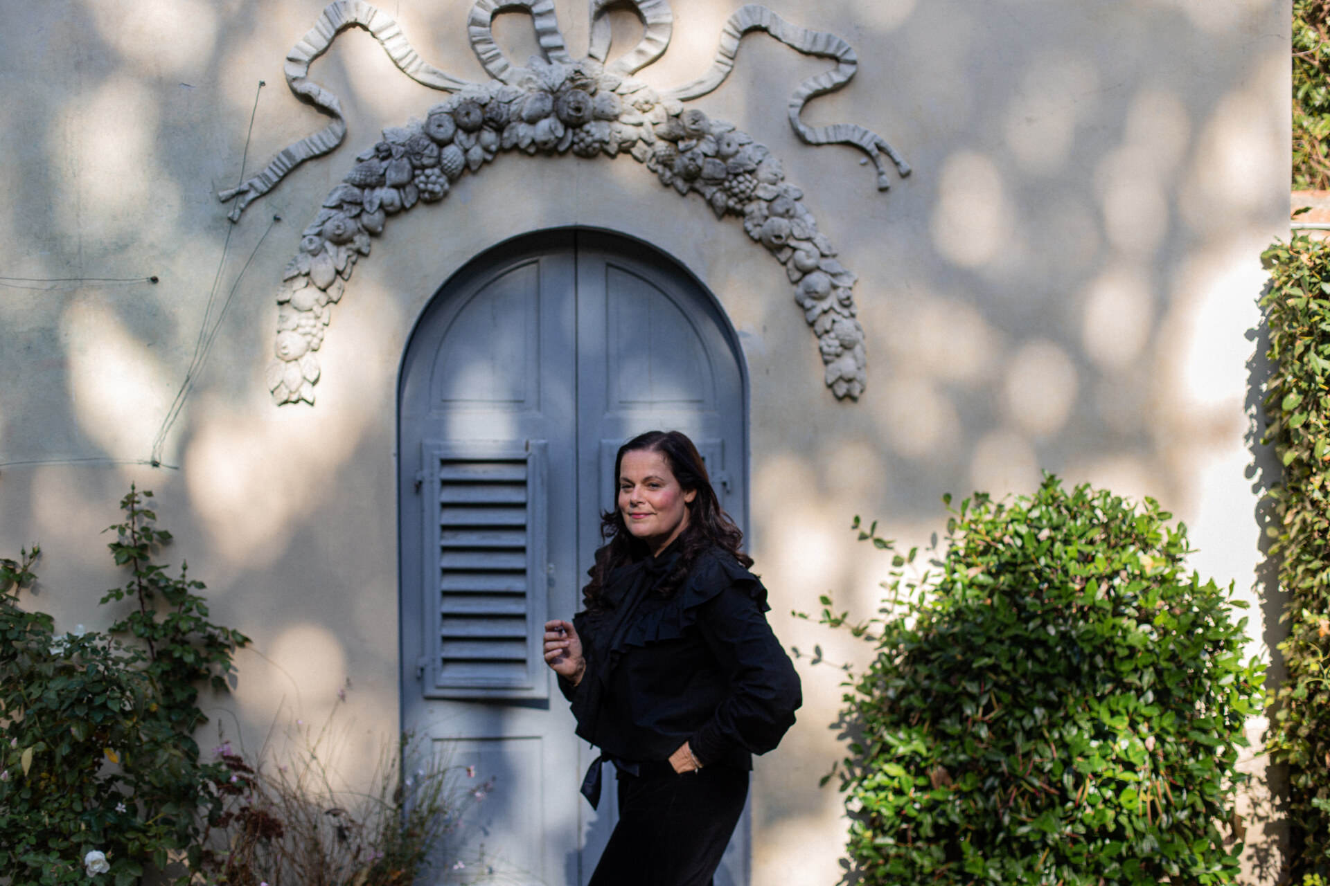 an image of a woman standing in front of a pale blue wooden door with ceramic fruit forming a frame around the top