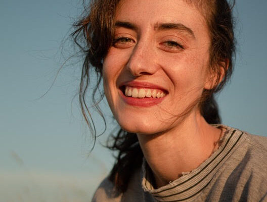 an image of a young girl smiling with her hair in a pony tail slightly blowing in the wind