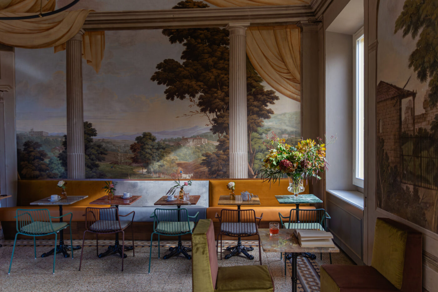 the breakfast room at stella d'italia with light shining into rows of tables in front of a vast mural of the countryside