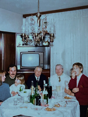 a vintage image of a family sitting around a dinner table with a fancy chandelier and a TV in the background