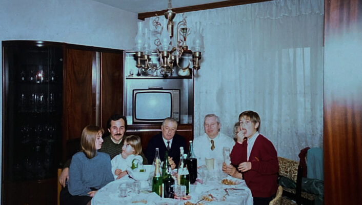 a vintage image of a family sitting around a dinner table with a fancy chandelier and a TV in the background