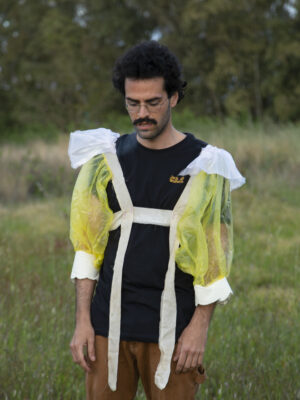 a man wearing a black t shirt and puffed sleeves standing in the grass and looking down