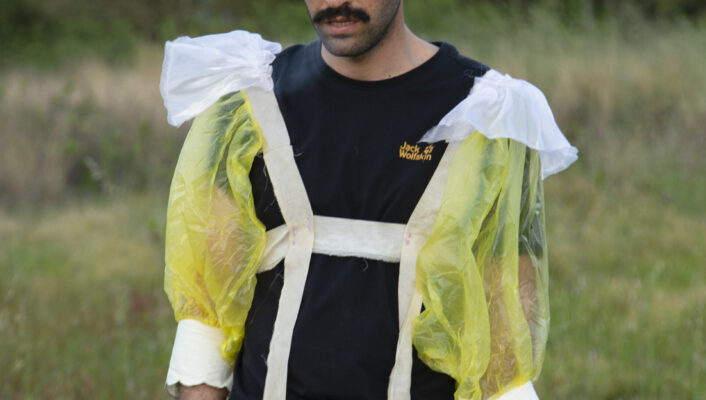 a man wearing a black t shirt and puffed sleeves standing in the grass and looking down
