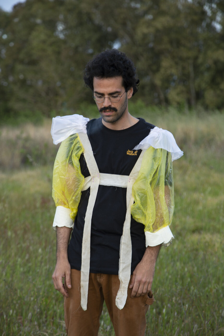a man wearing a black t shirt and puffed sleeves standing in the grass and looking down