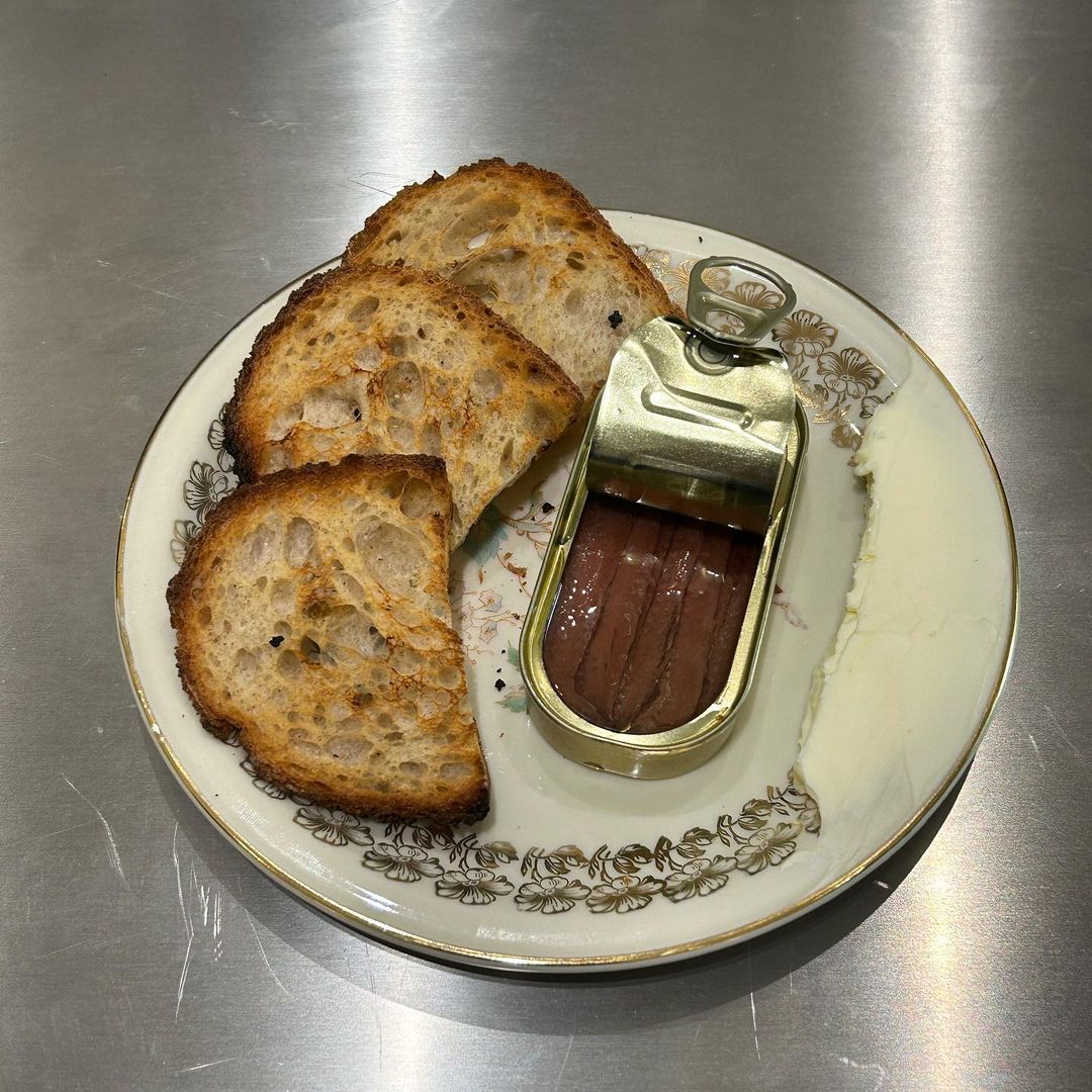 slices of bread on a china plate with an opened jar of anchovies at bar paradiso