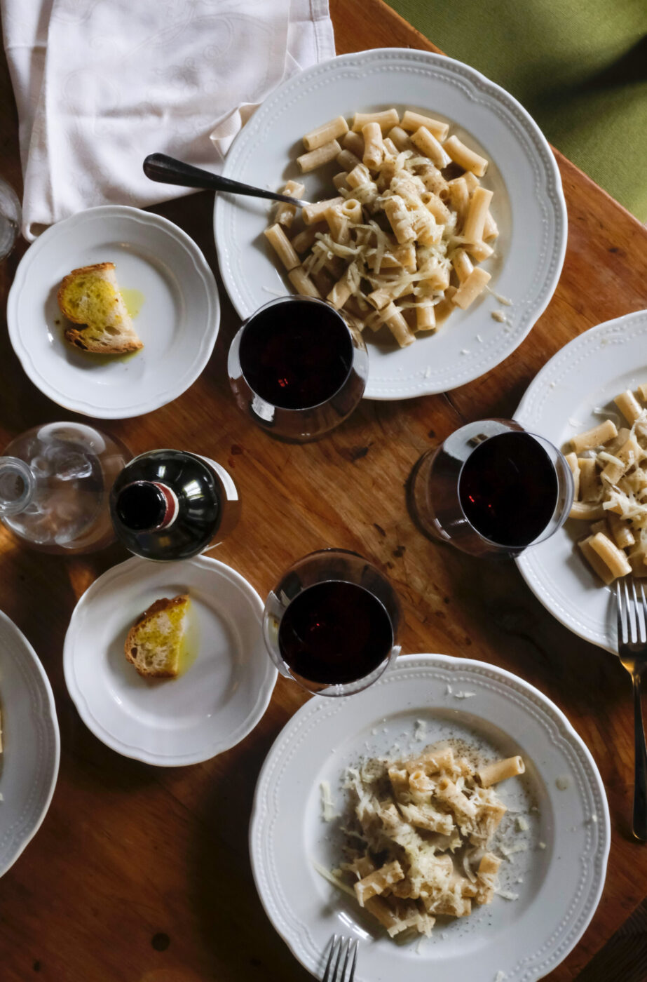 overhead shot of three plates of cacio e pepe rigatoni with red wine in glasses