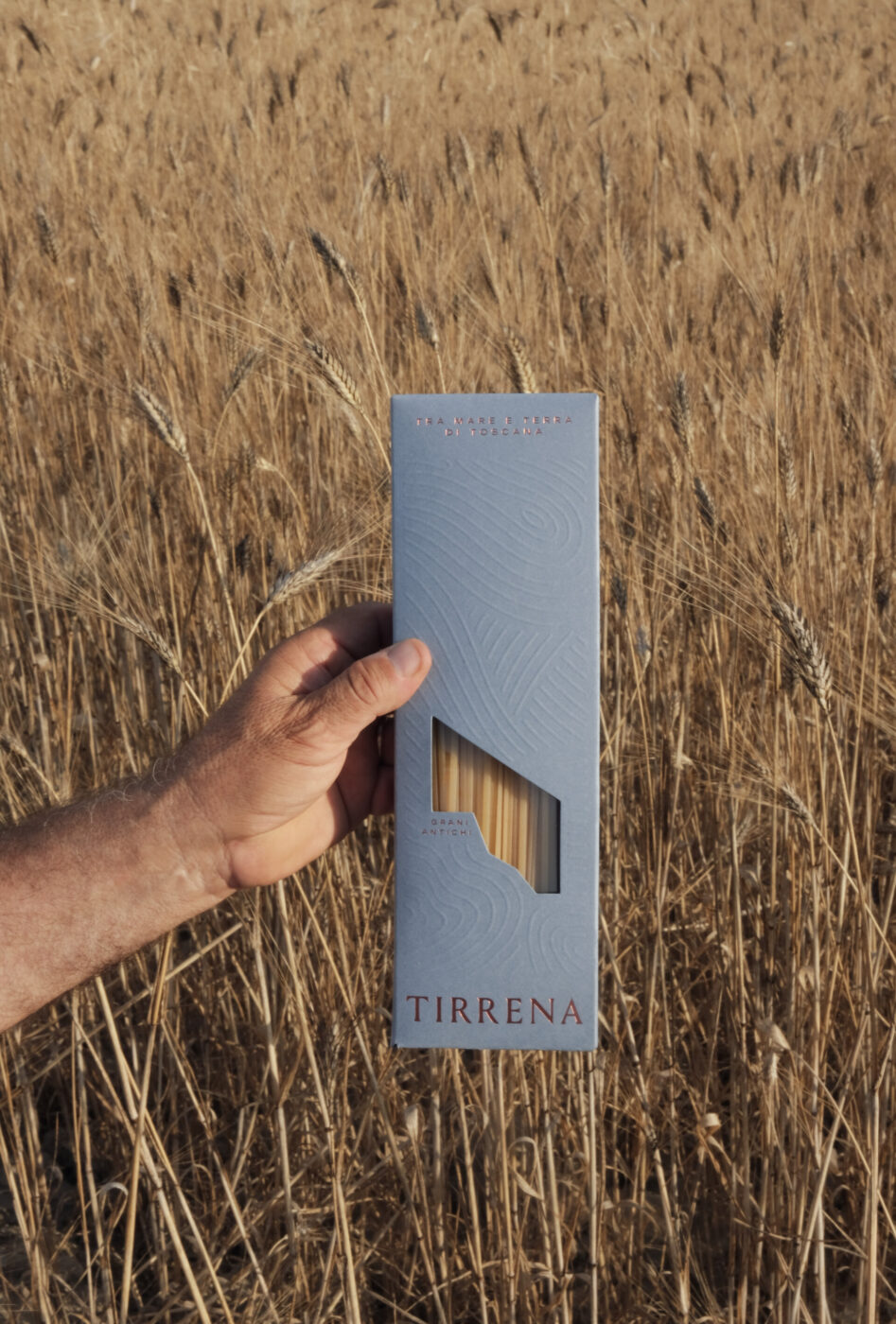 a man holding a box of tirrena spaghetti in a wheat field