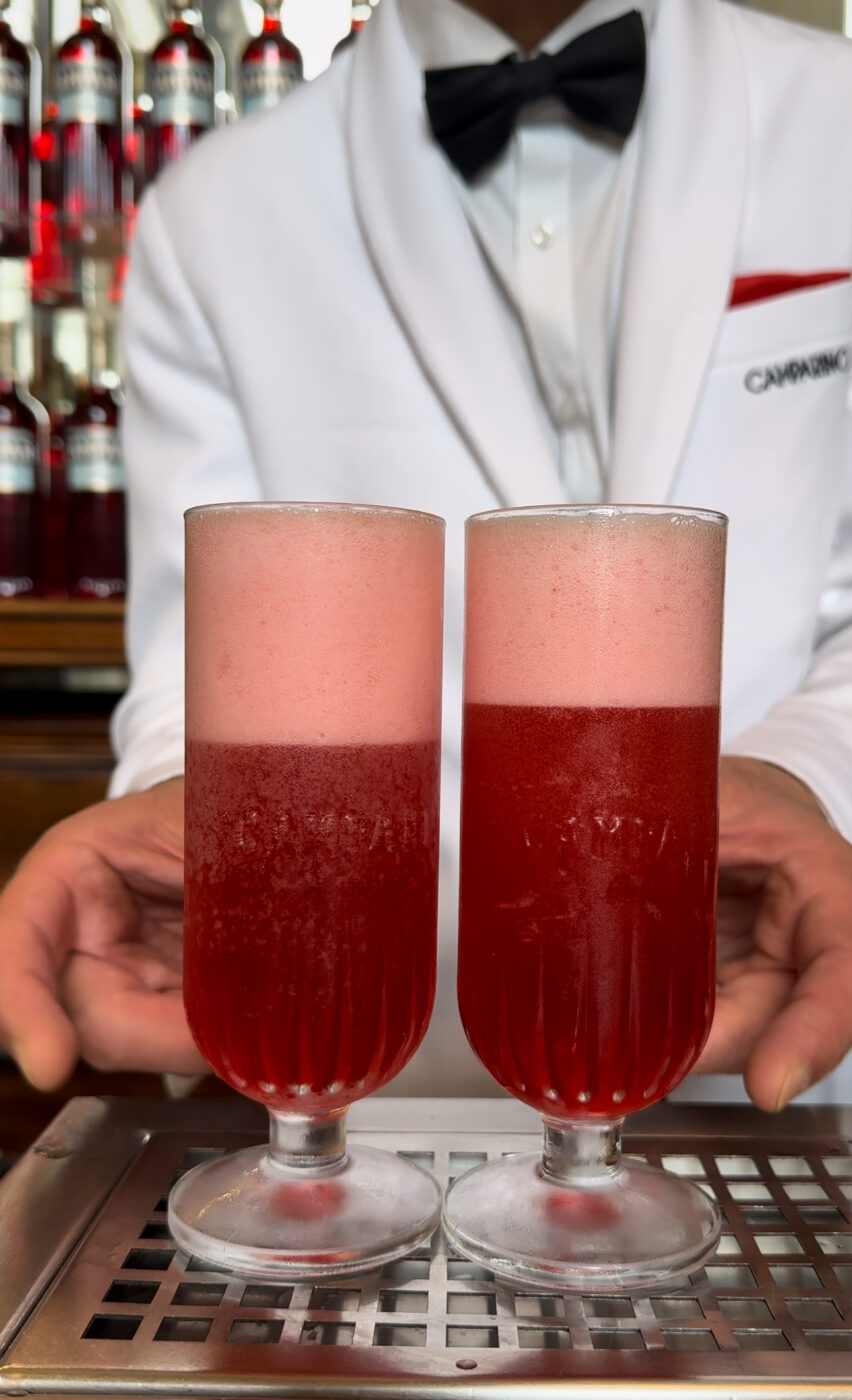 Two frothy glasses of Campari Seltz with a bow-tied waiter in the back from Camparino in Milan
