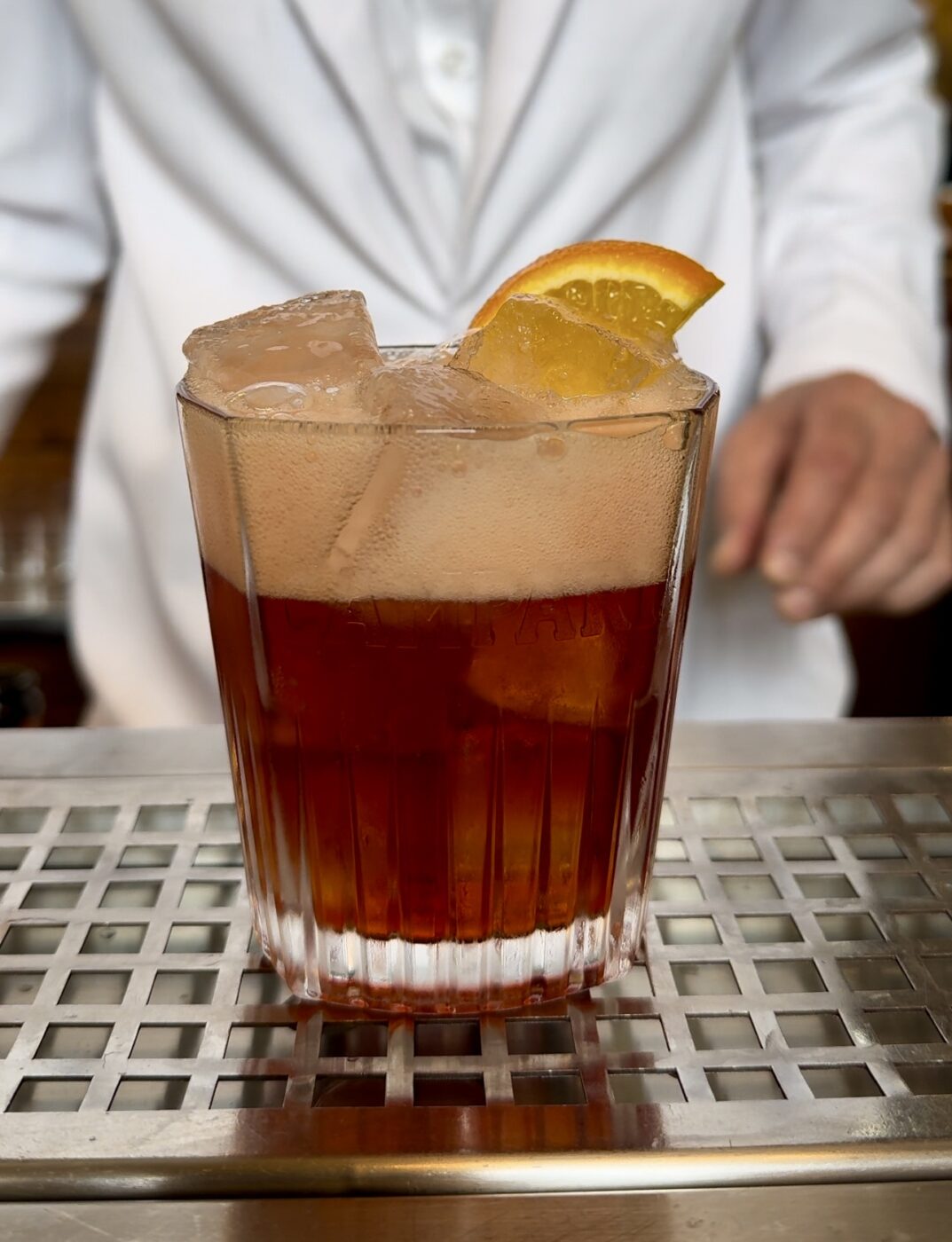 an americano cocktail on a bar with a white-suited waiter in the back