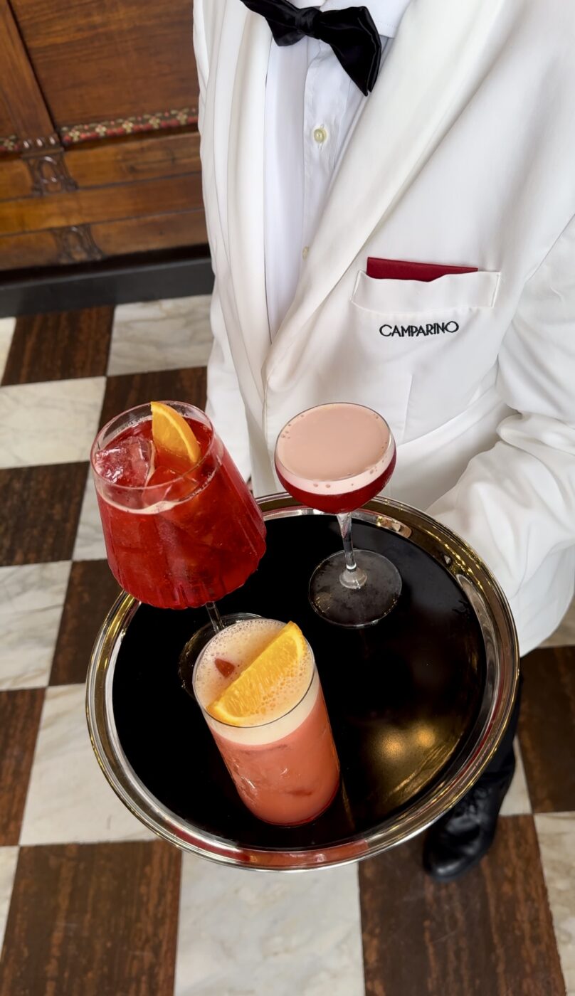 a bowtied waiter holding a tray of three campari cocktails at camparino in milan