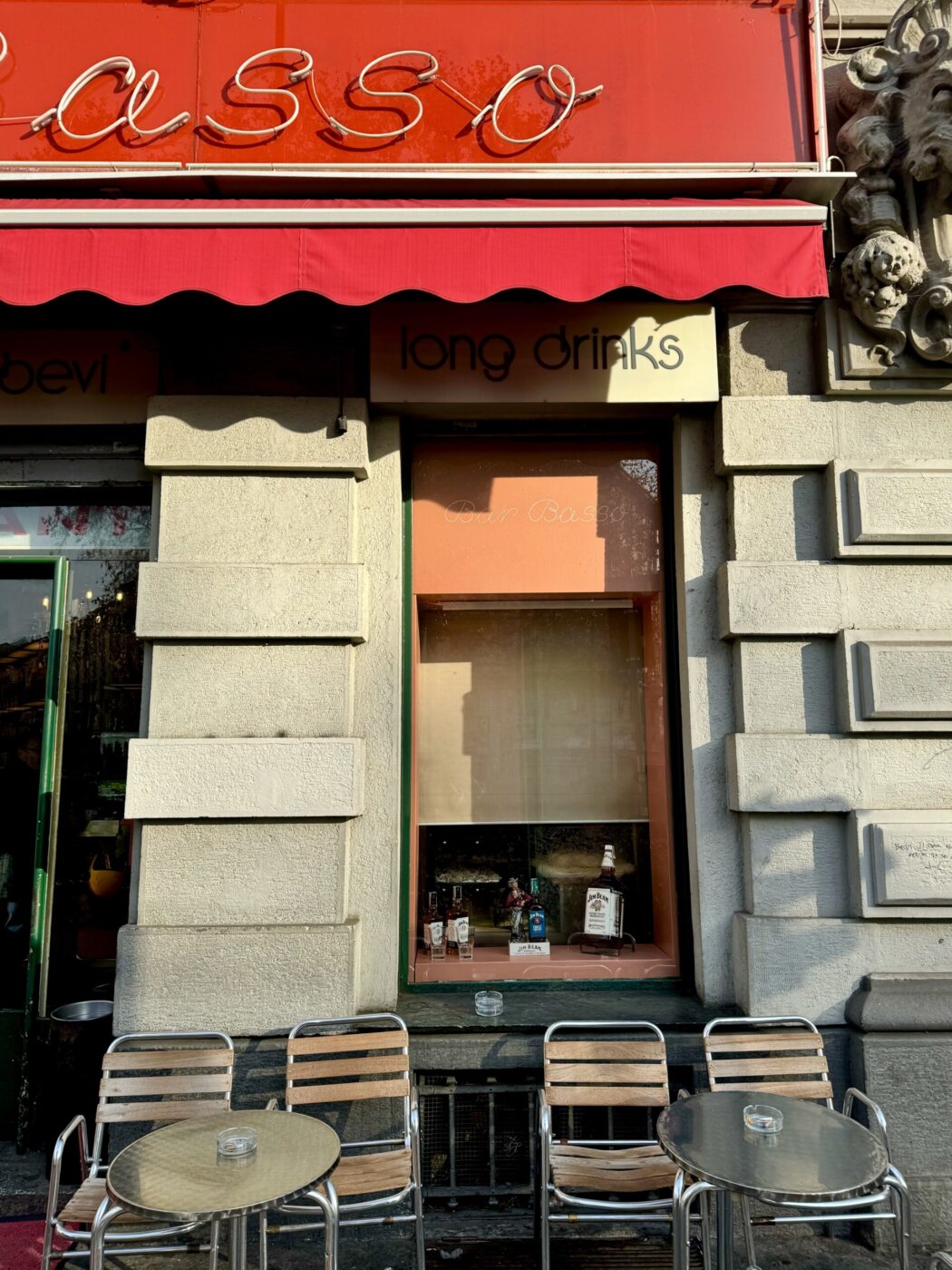 Two tables under the red awning of Bar Basso in Milan
