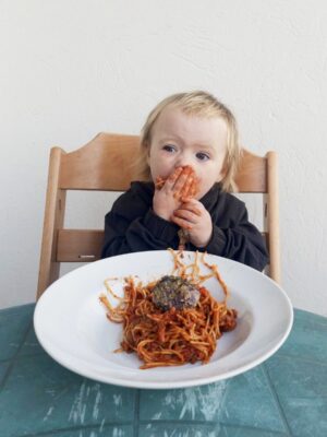 a little girl shoving a bite of spaghetti and meatballs in her mouth