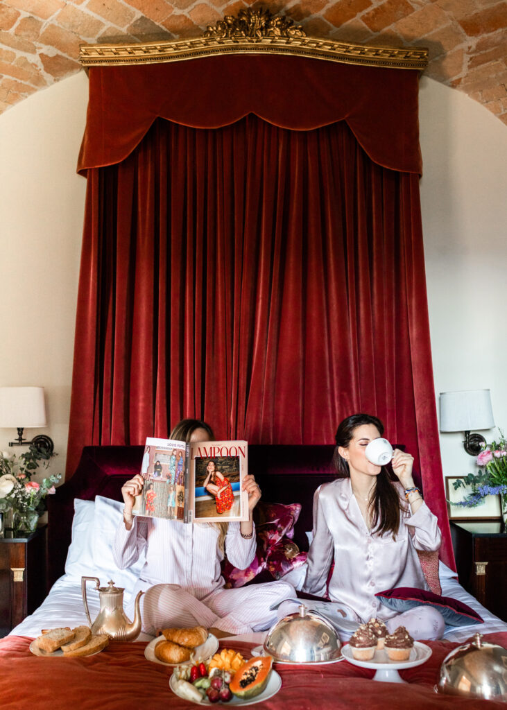 two girls enjoying breakfast in bed at Relais San Maurizio with a red velvet curtain headboard
