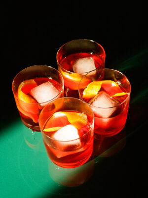 four negroni with a large ice cube on a green table
