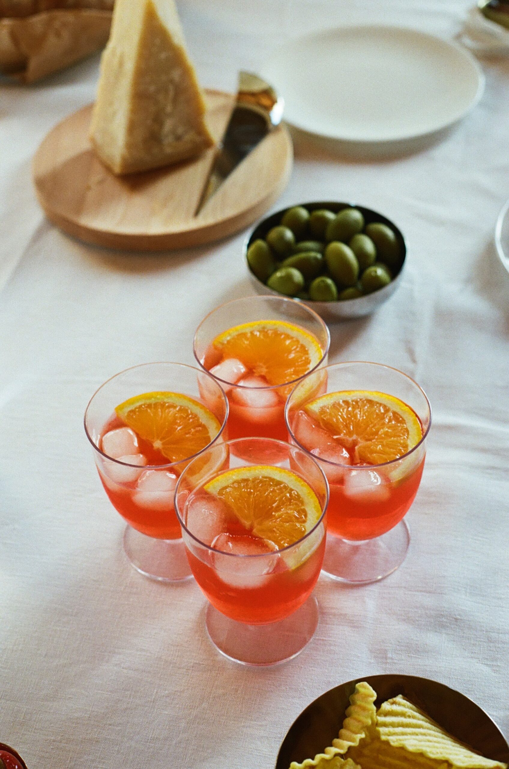 four spritzes on a table with olives and cheese