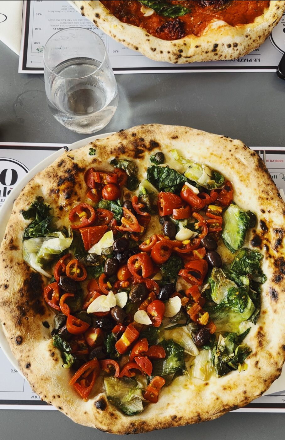 a pizza from 50 kalò with cherry tomatoes, olives, capers, and escarole