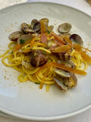 a white plate with spaghetti covered in clams and bottarga