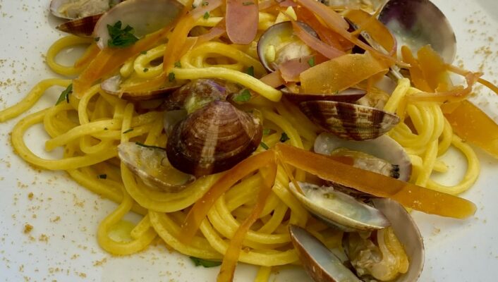 a white plate with spaghetti covered in clams and bottarga