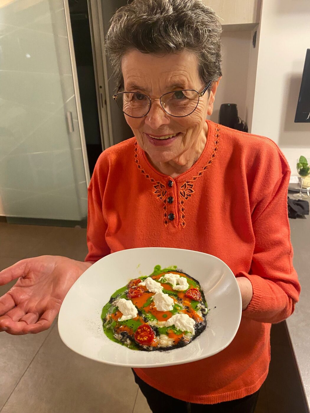 nonna holding a plate of risotto called risotto camouflaged as pizza from Mattia Agazzi at Gucci Osteria