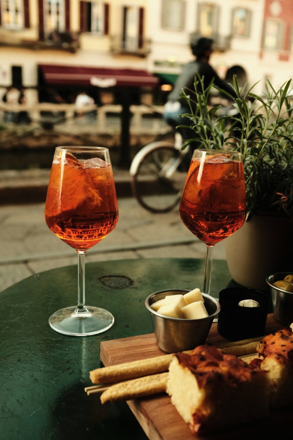 two spritzes on a green table with some focaccia and breadsticks and cheese