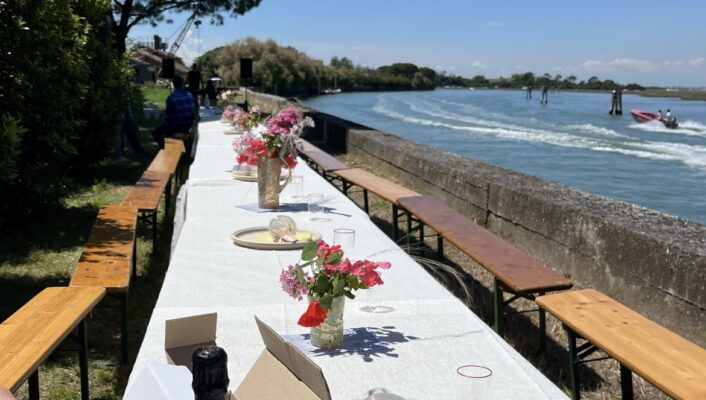 a long table set up along the water on an island by venice