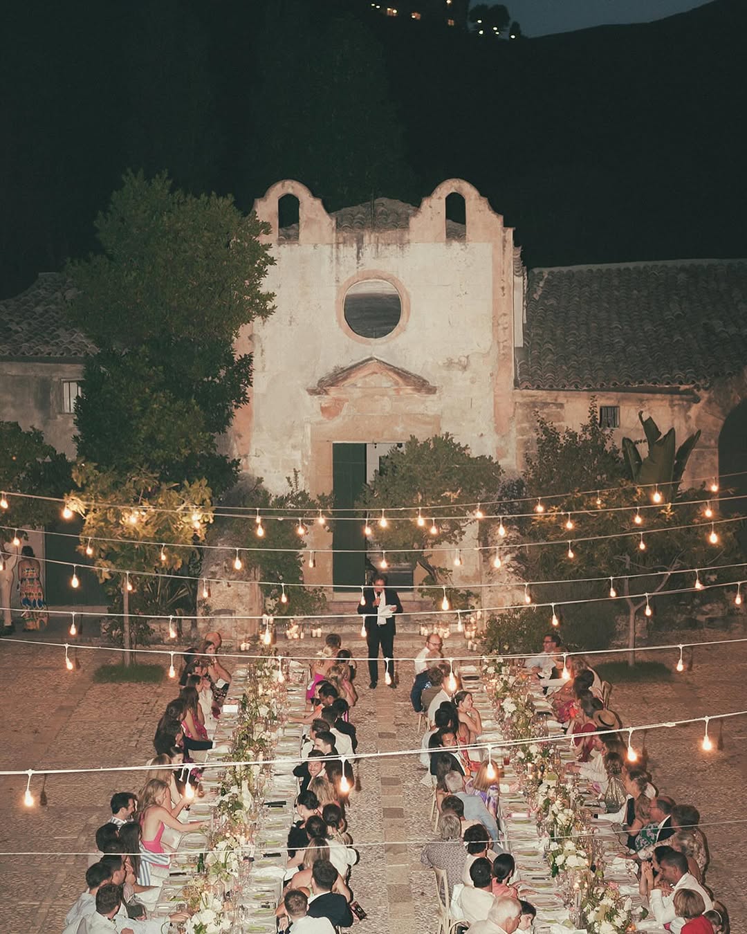 an overhead image of Tonnara di Scopello with large tables and fairy lights in the courtyard