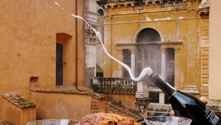 an image of a bottle of champagne popping on a balcony in Rome with panettone