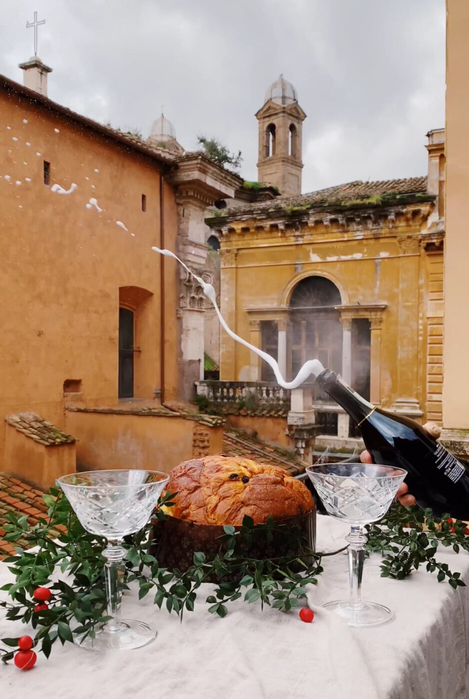 an image of a bottle of champagne popping on a balcony in Rome with panettone