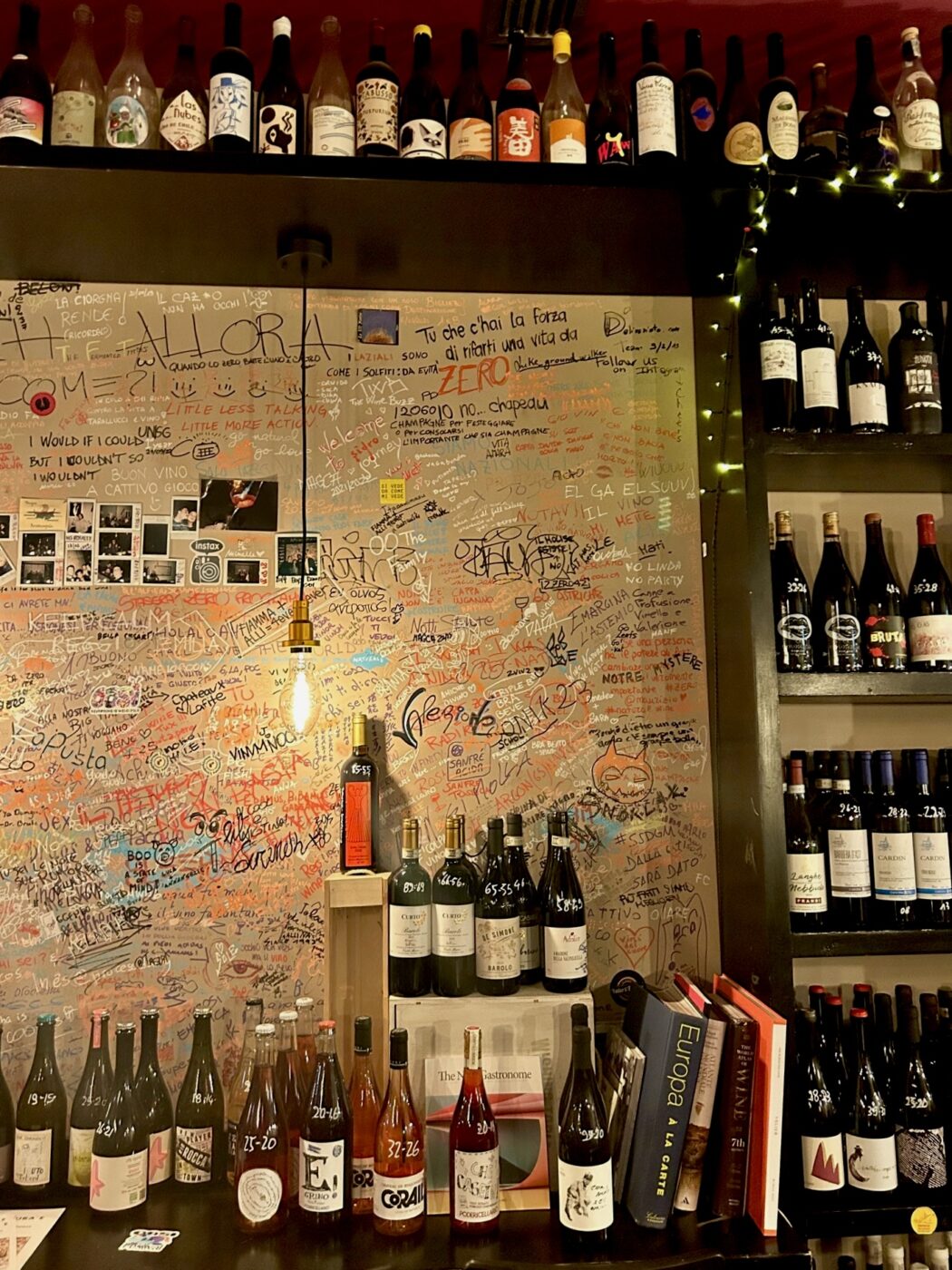 a wall covered with signatures and with bottles all around it from Zero Enoteca Conviviale in Bra
